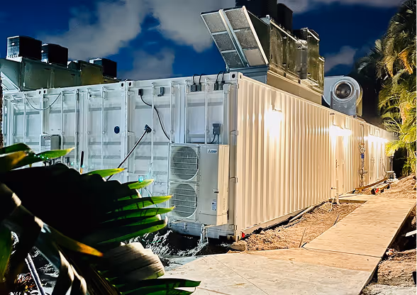 Large white portable industrial container unit with HVAC systems installed on a construction site at night.