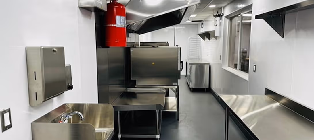 Clean modular commercial kitchen with stainless steel counters, sink, oven, and a red fire extinguisher.