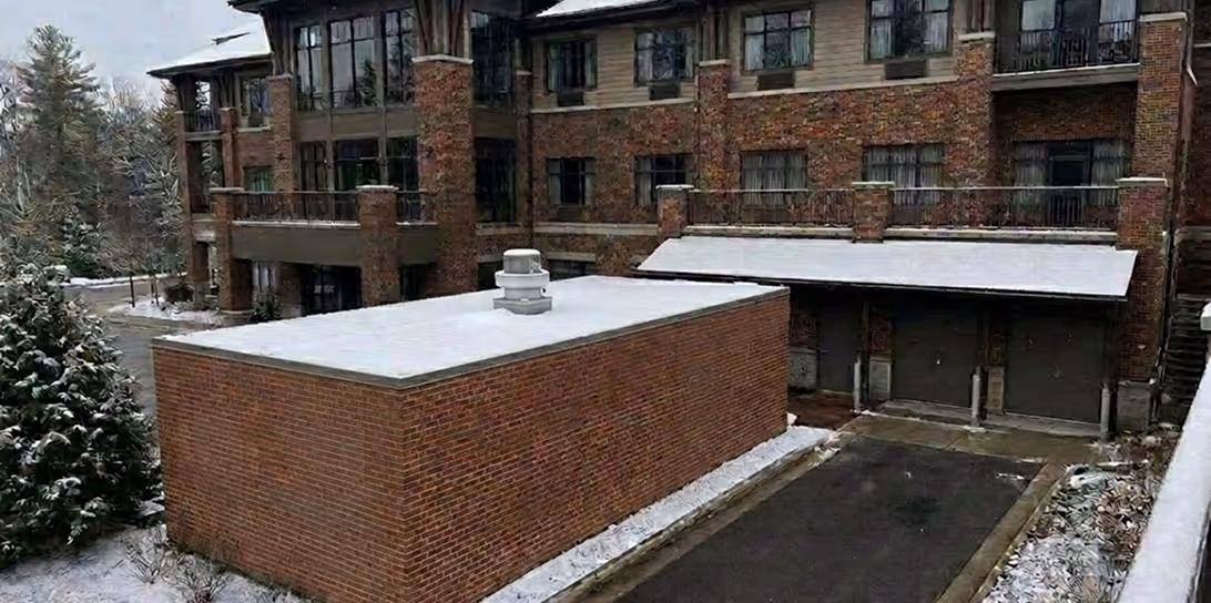 Snow dusting on brick buildings, pavement, and trees in a residential area on a cloudy day.