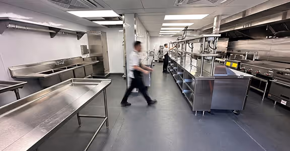 Two chefs walking in a clean, spacious commercial kitchen with stainless steel counters and appliances.