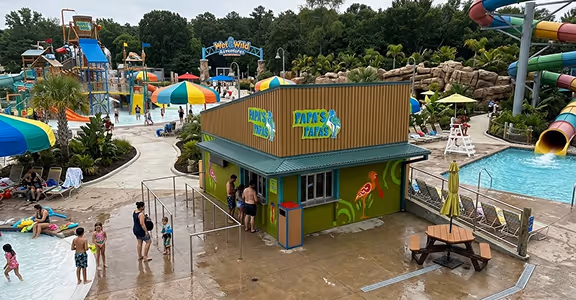 People at a colorful water park with slides, a quick service kitchen, and a pool area on a sunny day.