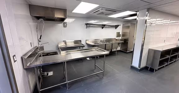 Clean commercial hotel kitchen with stainless steel sinks, prep tables, and storage shelves.