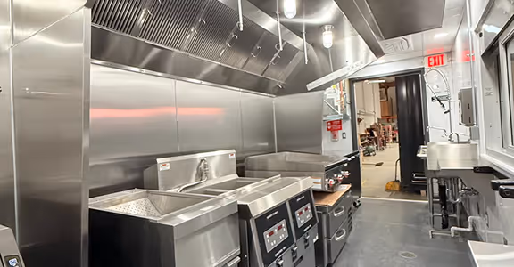 Interior of a clean fast-food kitchen with stainless steel appliances and ventilation hood.