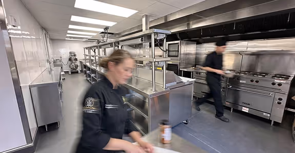 Busy commercial kitchen with chefs working near stainless steel appliances and cooking equipment.