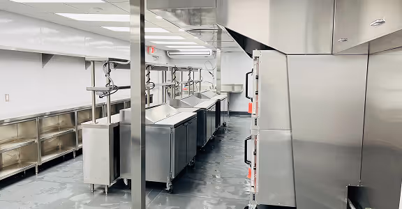 Modern commercial kitchen with stainless steel counters, ovens, and overhead exhaust ventilation.