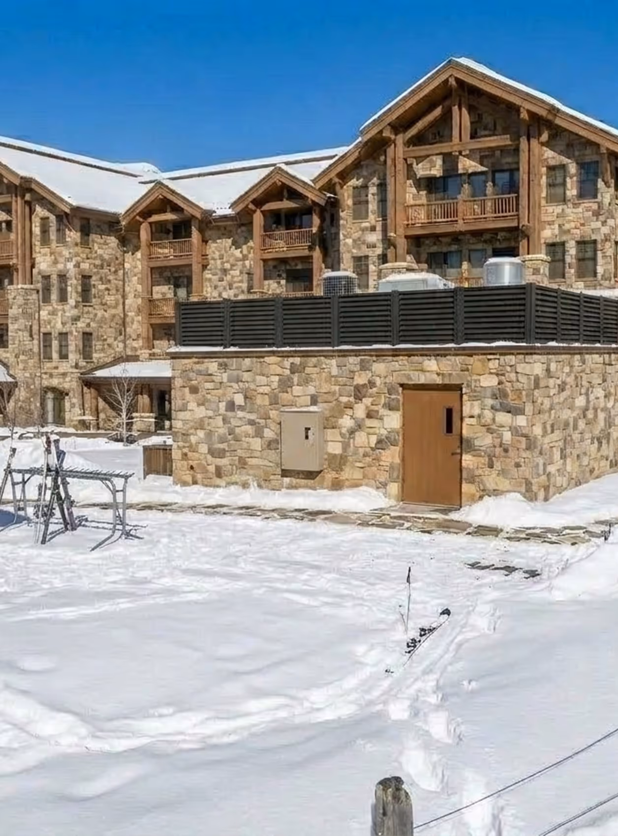 Snow-covered stone building with wooden door and balconies under clear blue sky.
