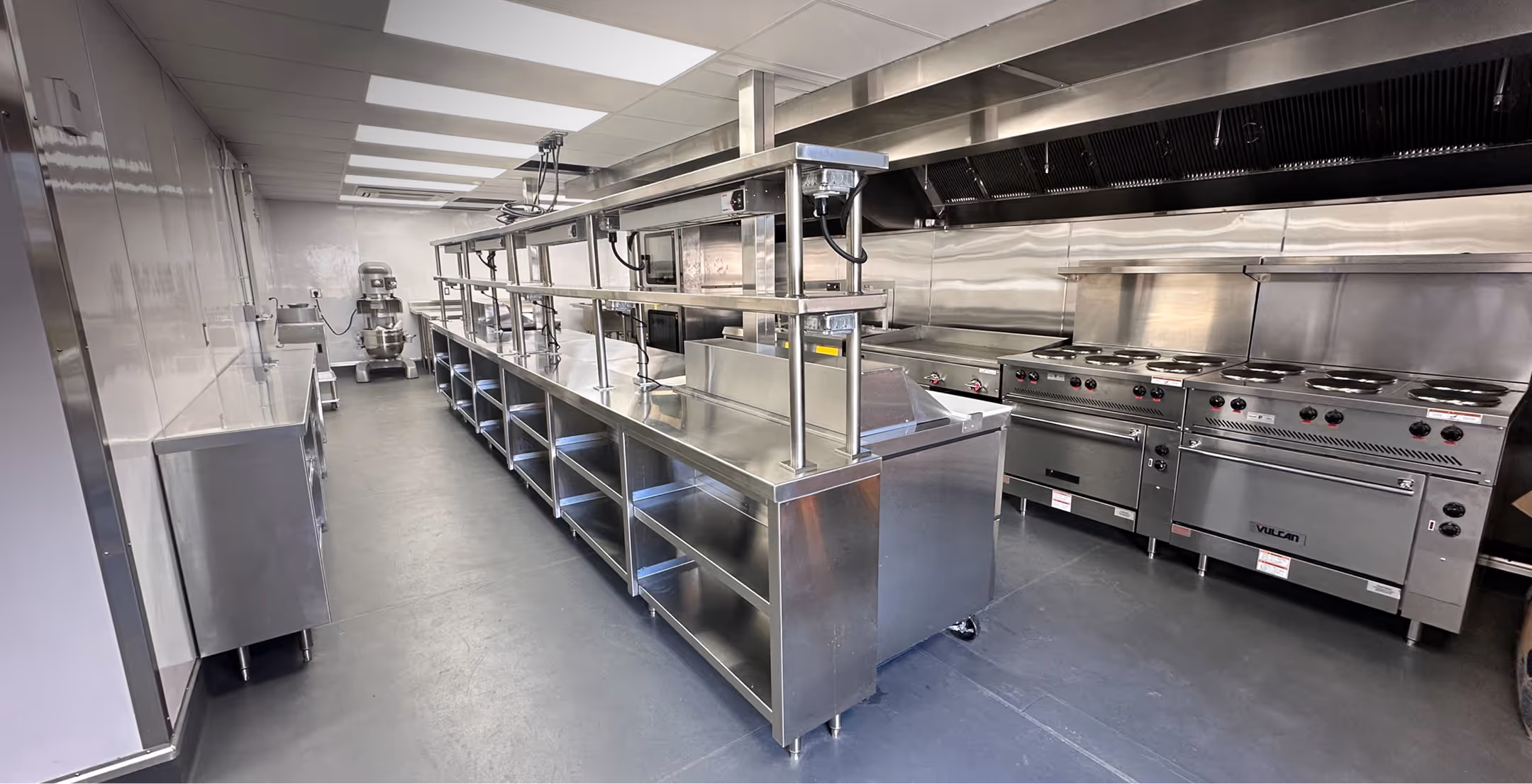 Modern commercial kitchen with stainless steel counters, ovens, and cooking equipment.