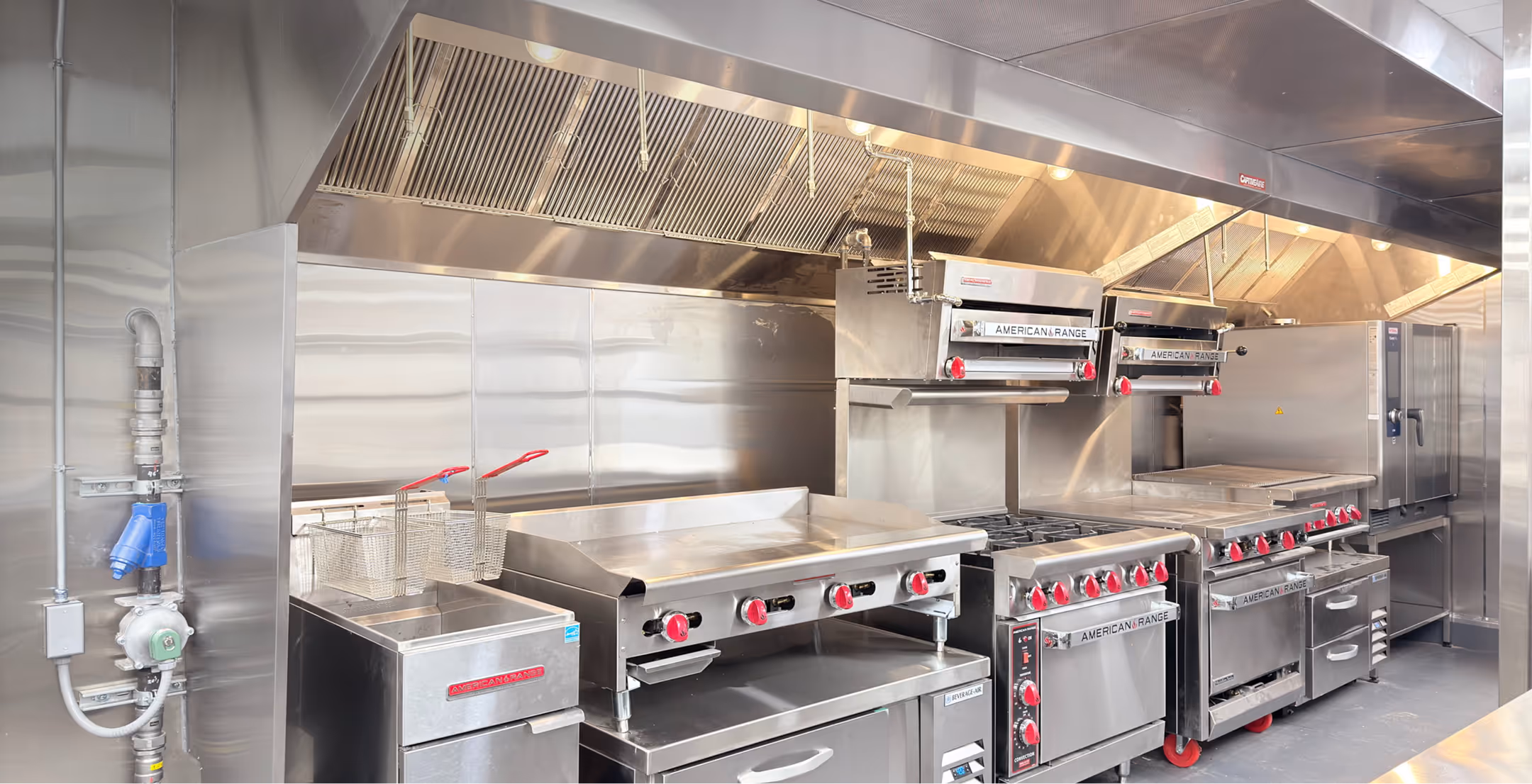 Commercial kitchen with stainless steel cooking equipment including fryers, griddles, ovens, and ventilation.