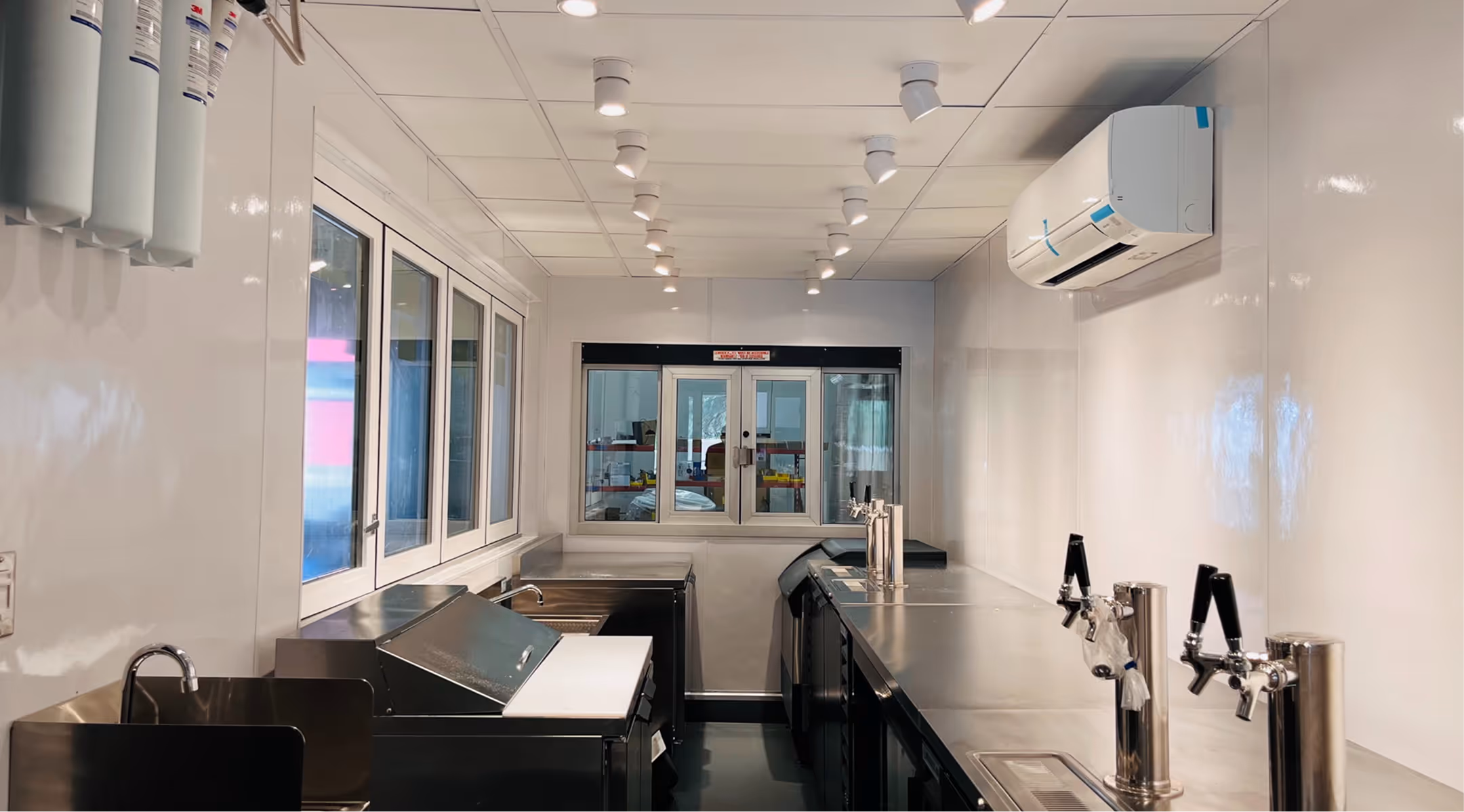 Modern quick service commercial kitchen with stainless steel counters and taps under bright ceiling lights.
