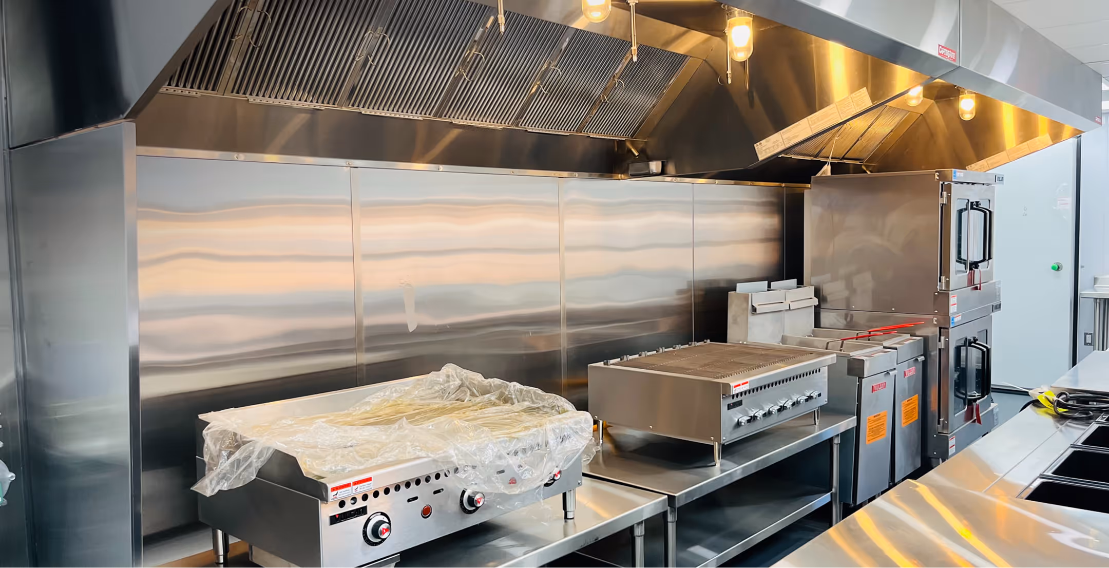 Modern quick service kitchen with stainless steel grill, oven, and ventilation hood.