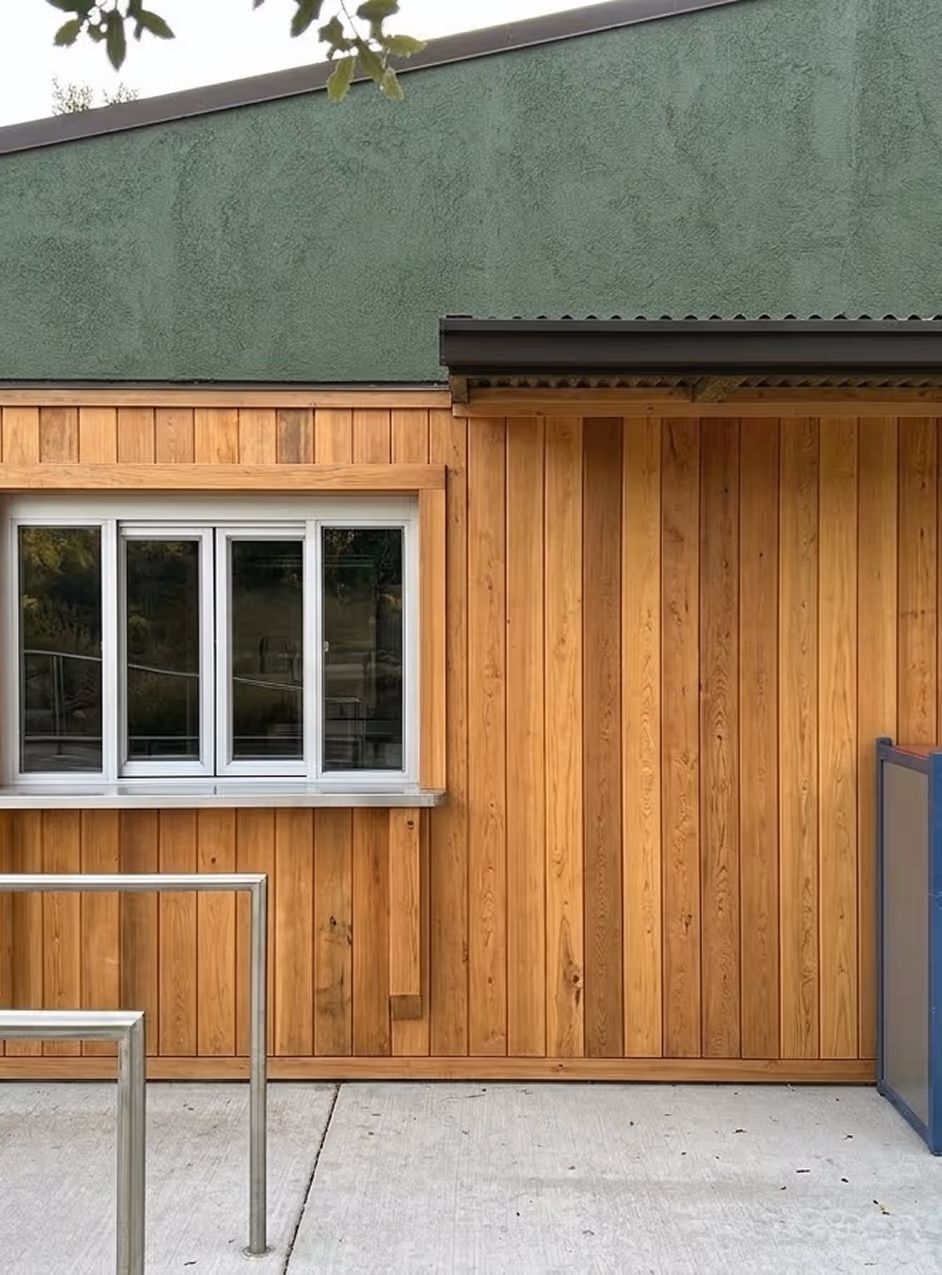 Building facade with vertical wooden panels, a sliding window, and metal railings on concrete ground.