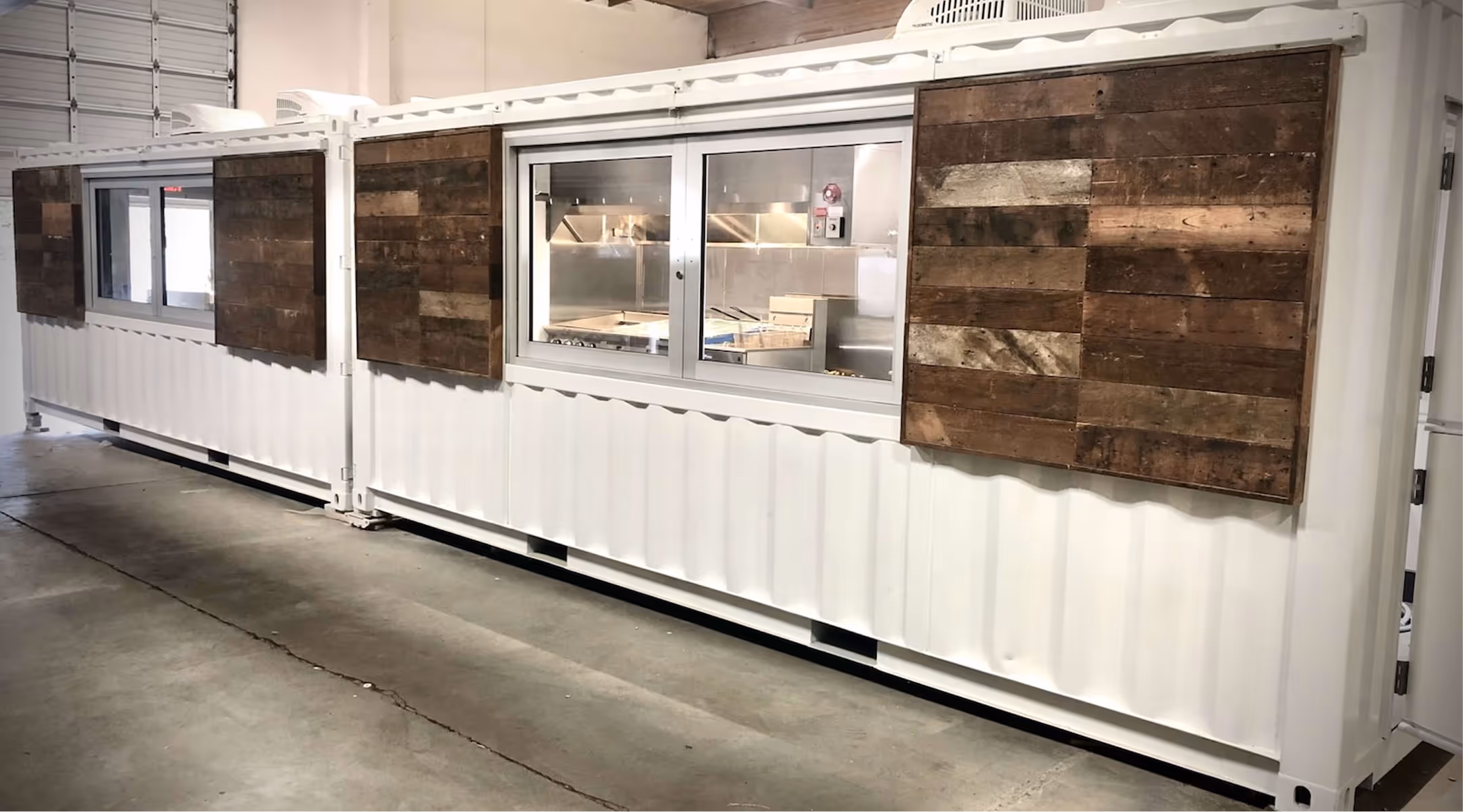 White shipping container converted to kitchen with wooden shutters and sliding windows.