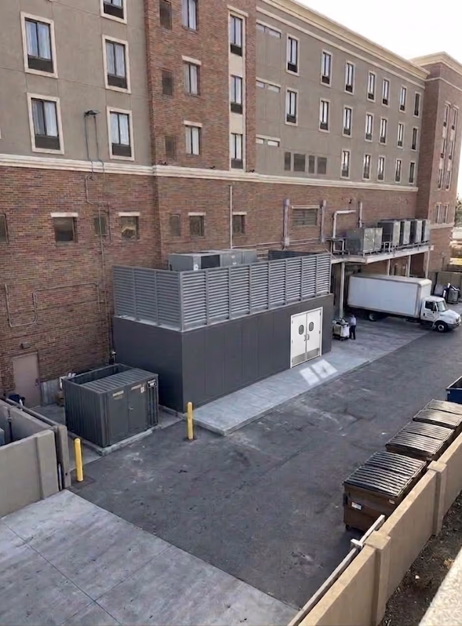 Loading dock area behind brick building with trucks, dumpsters, and industrial equipment.