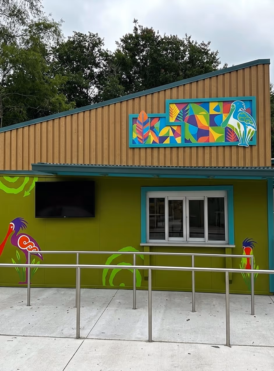 Colorful commercial fast food kitchen with bird murals, a service window, and a blank TV screen mounted outside.