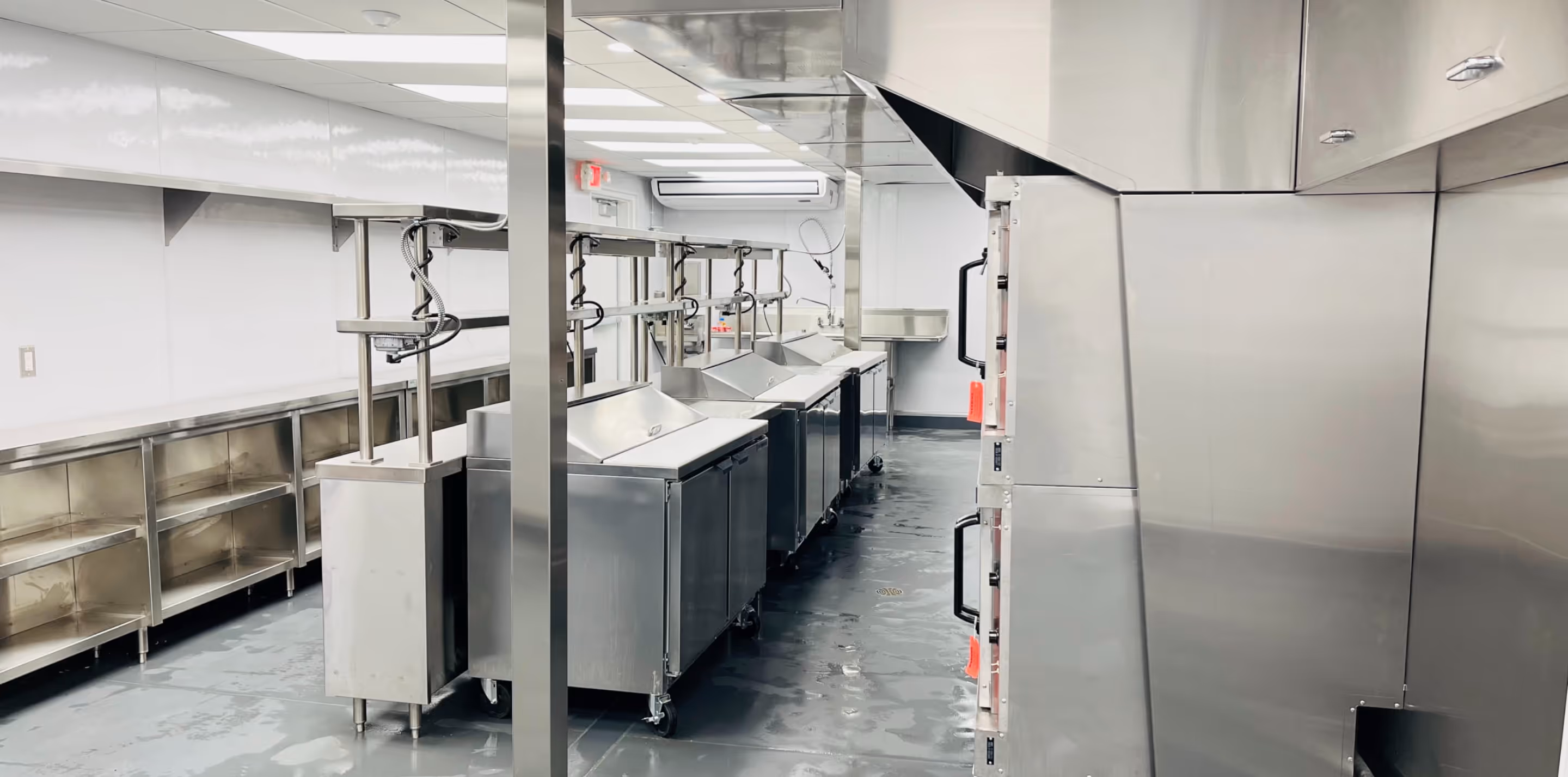 Modern commercial kitchen with stainless steel counters, storage shelves, and ventilation hoods.