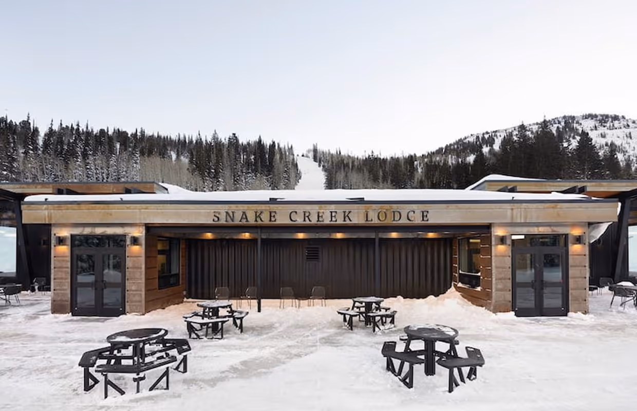 Snow-covered modular kitchen lodge in front of seating with tables and chairs in front of Snake Creek Lodge in a mountain setting.