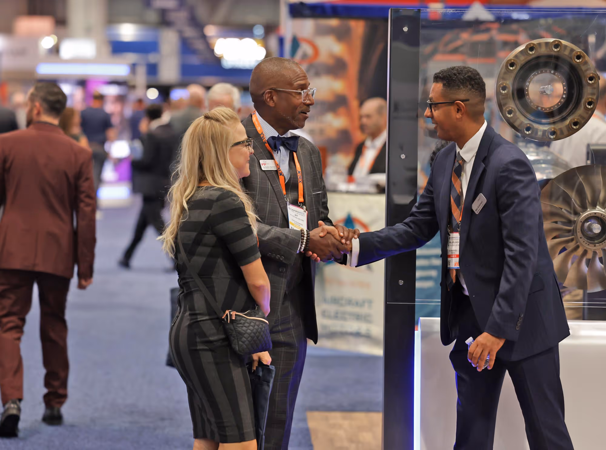 Three people in business attire shaking hands and talking on the 2025 NBAA-BACE exhibit floor