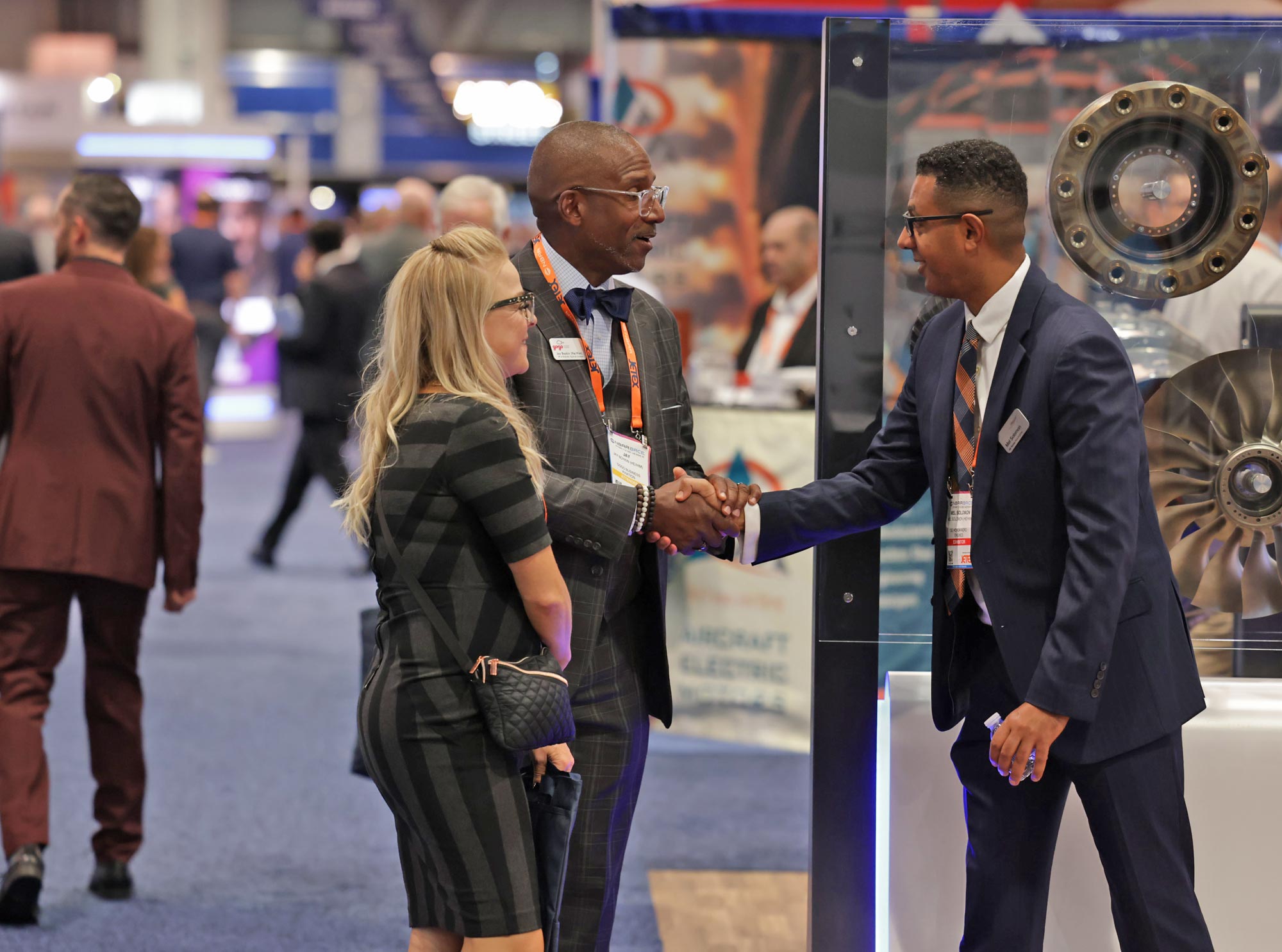 Three people in business attire shaking hands and talking on the 2025 NBAA-BACE exhibit floor