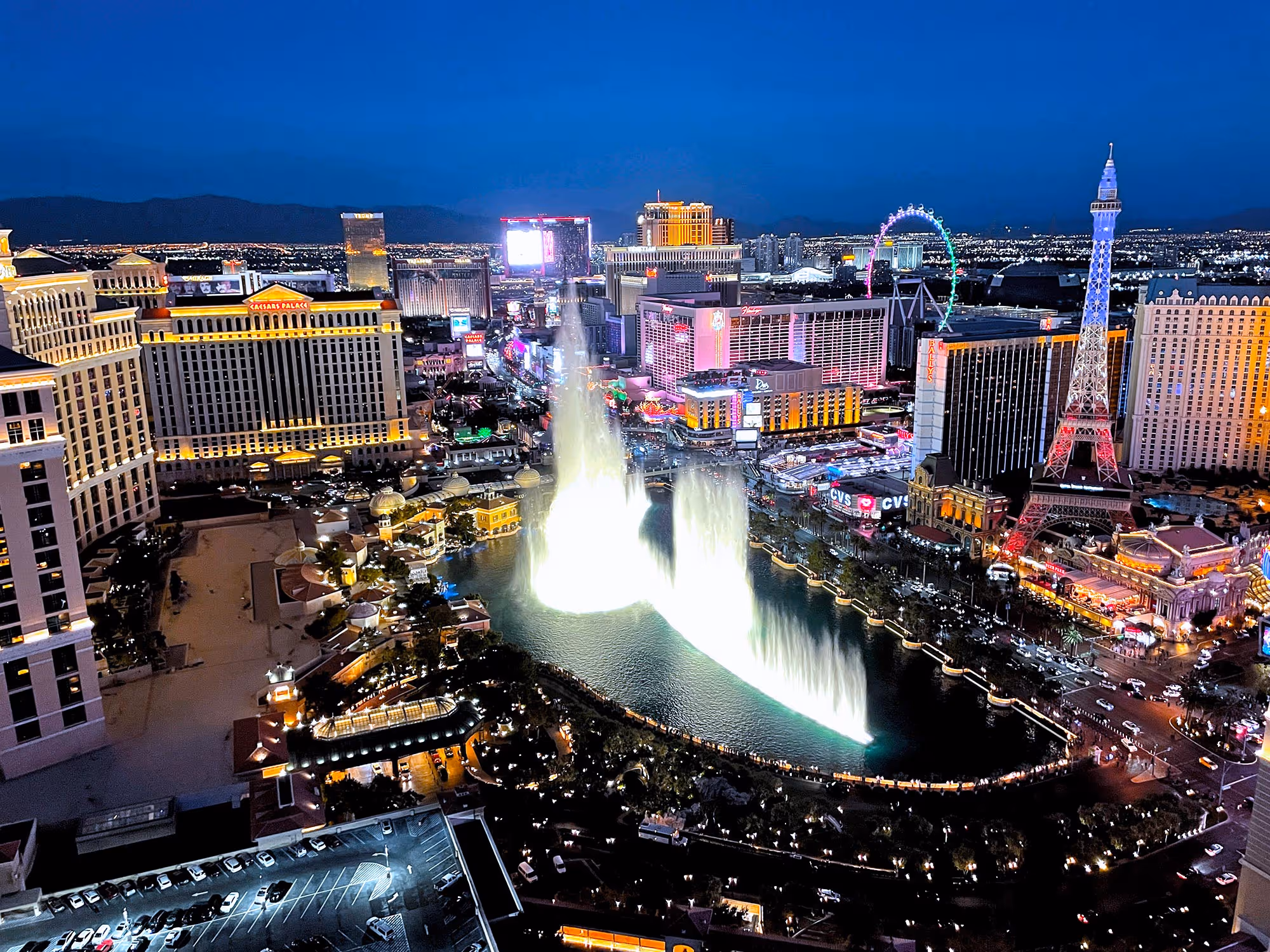 Night view of Las Vegas Strip with Bellagio fountain show and replica Eiffel Tower lit in colors.
