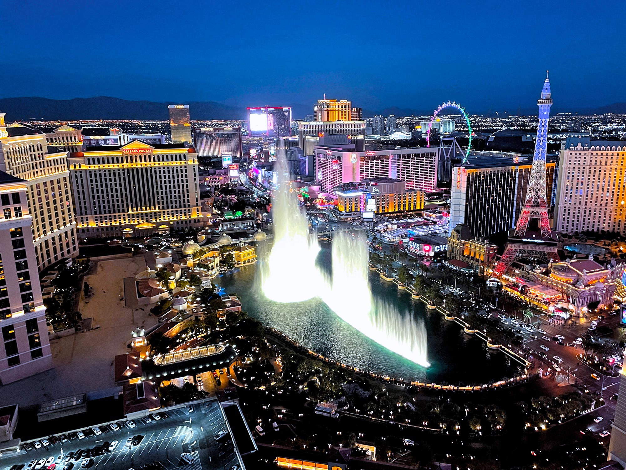 Night view of Las Vegas Strip with Bellagio fountain show and replica Eiffel Tower lit in colors.