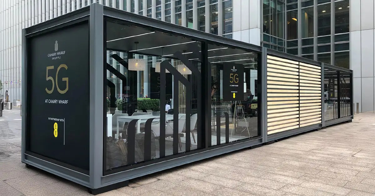 Showblock glass container office with 5G Canary Wharf branding and seating inside urban plaza