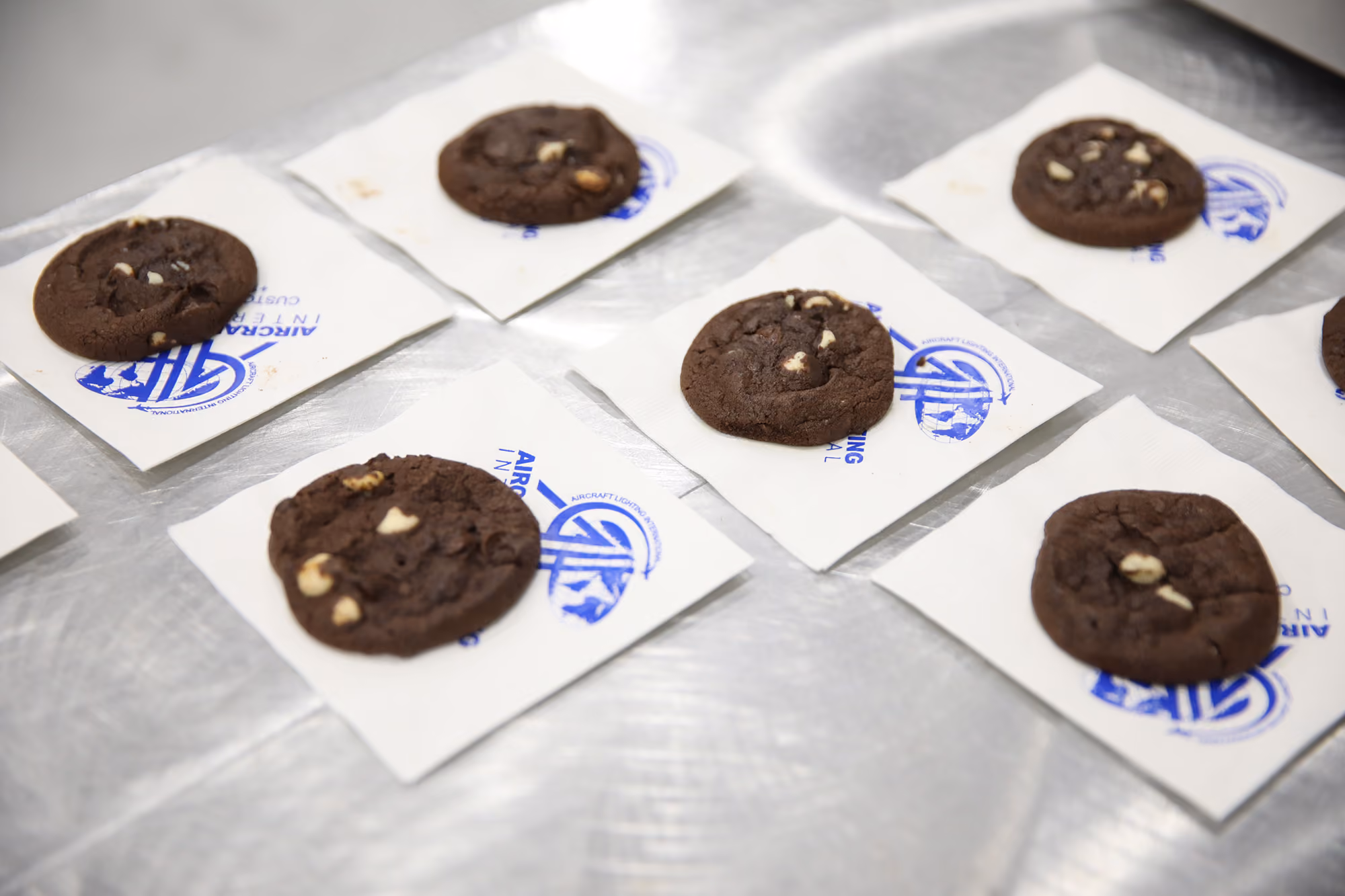 Chocolate cookies with white chocolate chips placed individually on white napkins featuring the Aircraft Lighting International logo