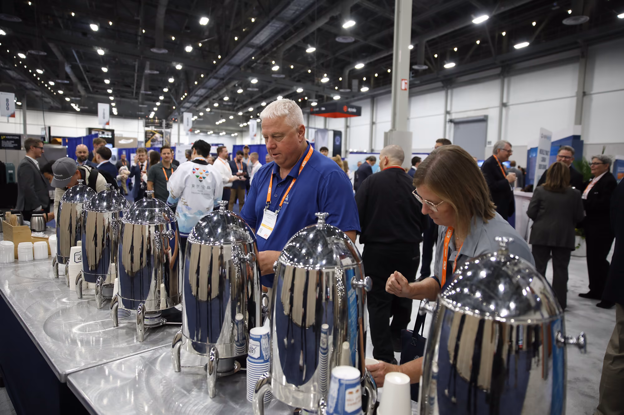 People serving themselves coffee from multiple stainless steel coffee urns at the 2025 NBAA-BACE Coffee Social