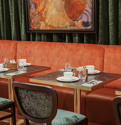 Elegant dining area with an orange velvet banquette, black marble tables, and green fabric chairs.