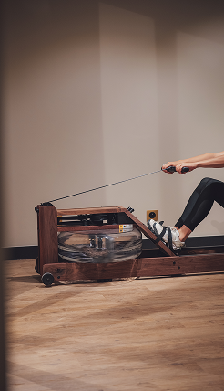 Personne en tenue de sport utilisant un rameur en bois dans une salle de sport avec un sol en bois clair.