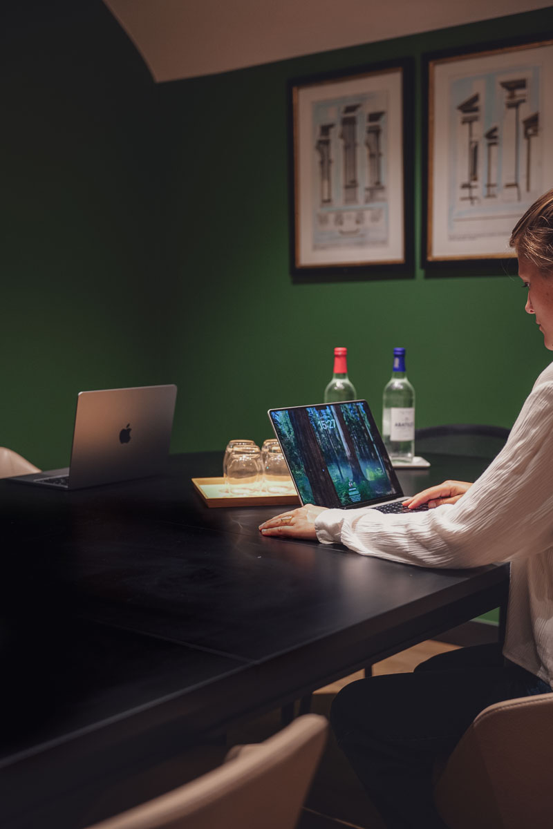 Personne travaillant sur un ordinateur portable dans une salle de réunion avec une table noire, des bouteilles d'eau et des verres.