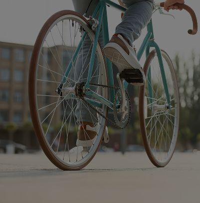 Personne pédalant sur un vélo de ville vert en surface urbaine avec bâtiments flous en arrière-plan.