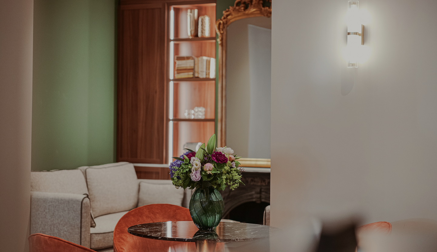 Bouquet de fleurs colorées dans un vase vert sur une table en marbre dans un salon moderne avec un canapé beige et un miroir doré.