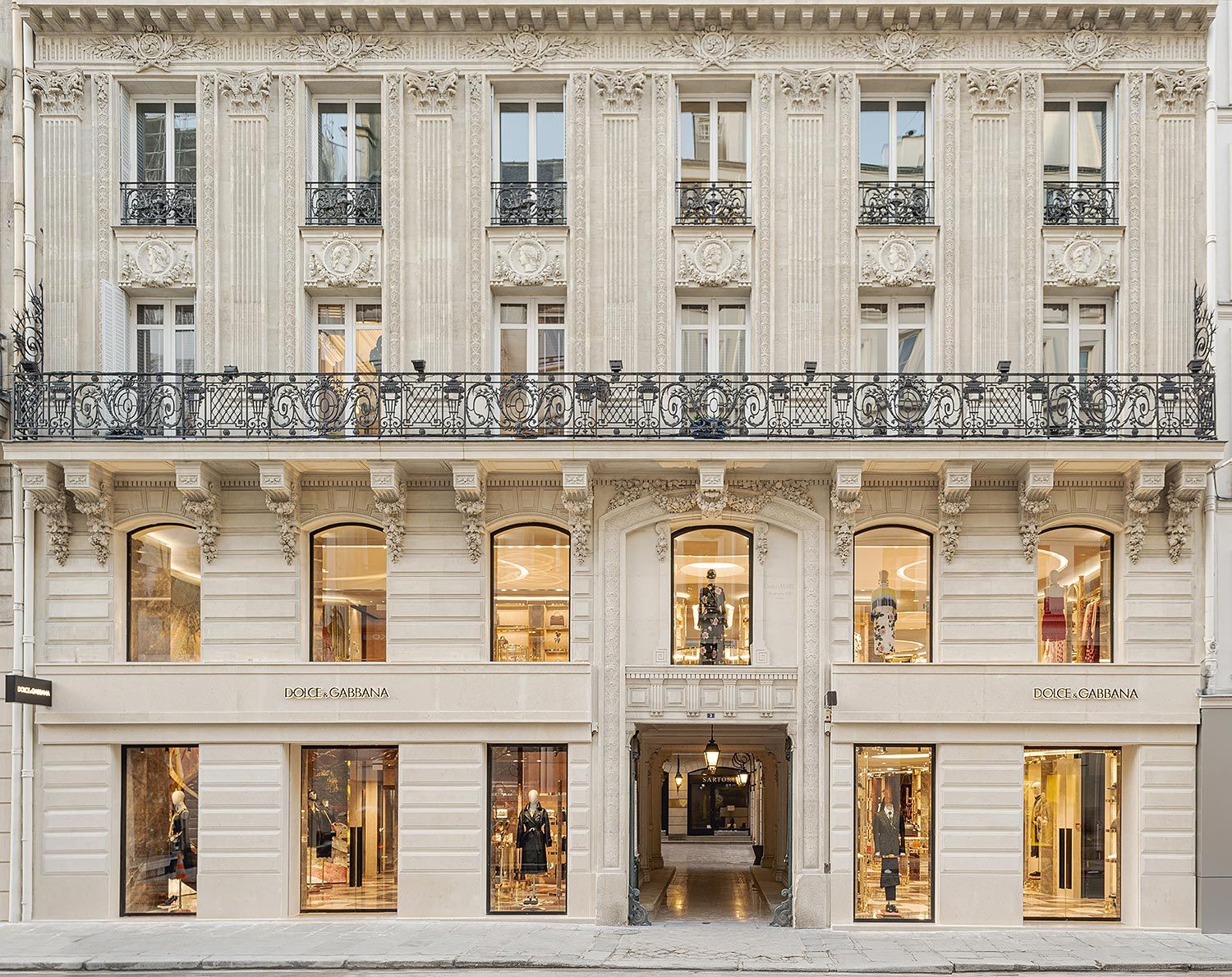 Façade en pierre classique d'un magasin Dolce & Gabbana avec grandes vitrines affichant des mannequins et un balcon en fer forgé au-dessus.