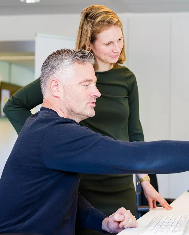 Twee volwassenen kijken samen naar een computerscherm, waarbij de man iets aanwijst terwijl de vrouw toekijkt.