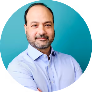 Portrait of a smiling man with a trimmed beard wearing a light blue shirt against a teal circular background.