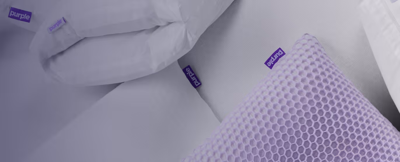 Close-up of white bedding and a purple gel cushion with hexagonal pattern, all branded with Purple tags.