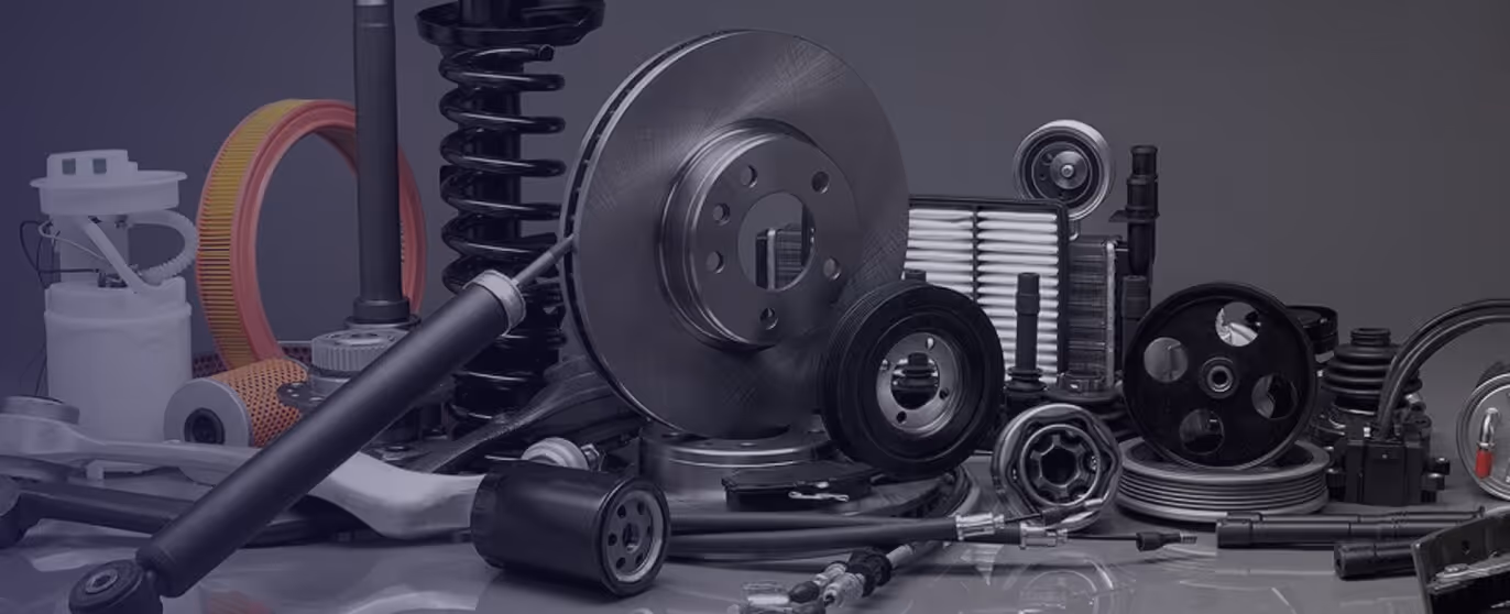 Collection of various automotive parts including a brake disc, shock absorber, air filters, and belts displayed on a reflective surface.
