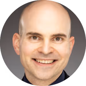 Smiling bald man with light skin and brown eyes against a gray background.