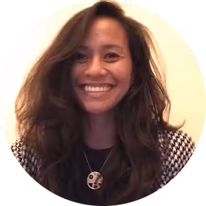 Smiling woman with long wavy dark hair wearing a black and white houndstooth jacket and a pendant necklace.