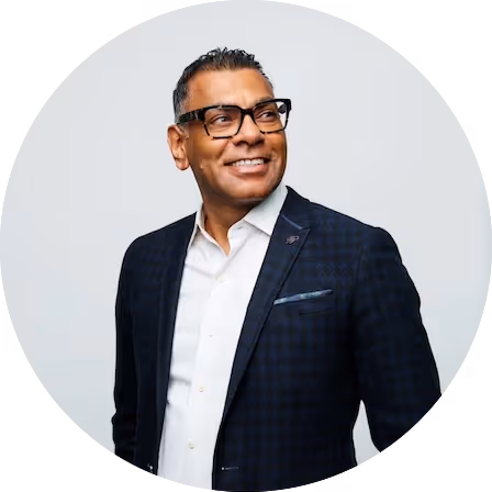 Smiling man with glasses wearing a dark checkered blazer and white shirt, looking to his left.