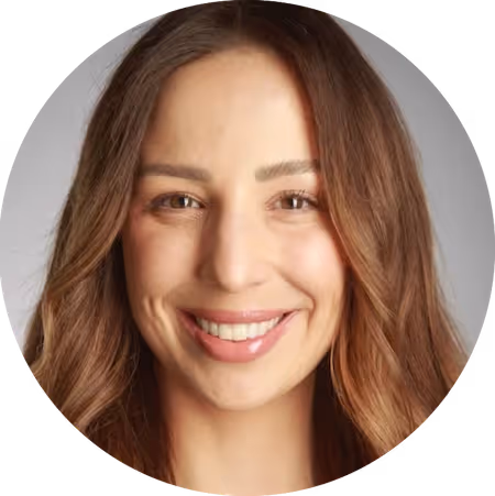 Smiling woman with wavy brown hair and light makeup against a plain background.