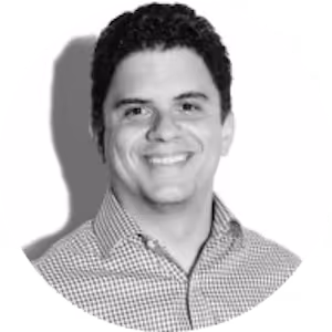 Smiling man with short dark curly hair wearing a checkered button-up shirt on a white background.