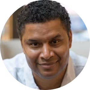 Portrait of a man with curly hair and a slight smile wearing a white shirt.