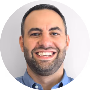 Smiling man with short dark hair and beard wearing a blue collared shirt.