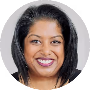 Smiling woman with shoulder-length black hair and purple lipstick against a neutral background.