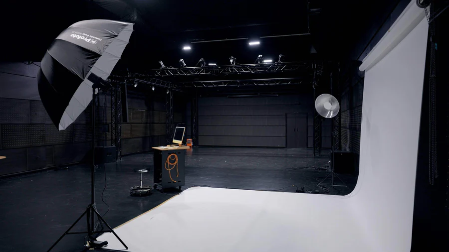 Fotostudio med lysutstyr, hvit bakgrunn og et bord med datamaskin i et stort rom.