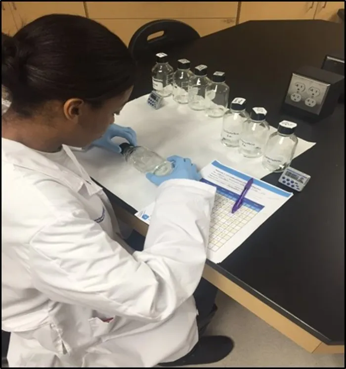 Scientist in white lab coat and blue gloves conducting laboratory experiment with glass bottles