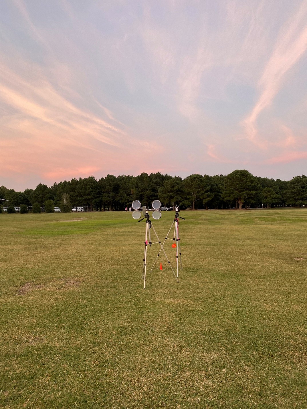 Weather monitoring equipment on grassy field at sunset with trees in background