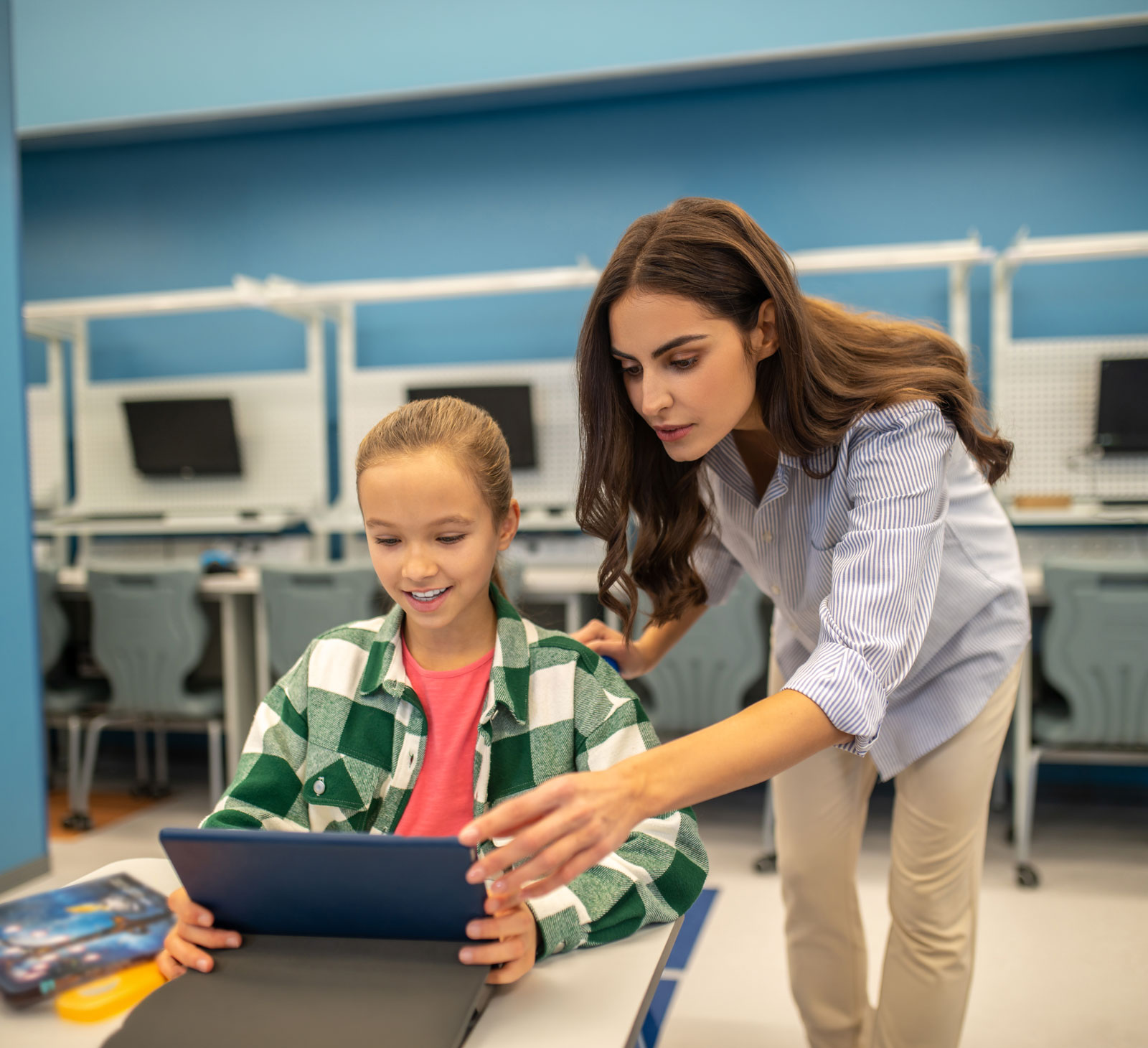 A woman helps a smiling child use a laptop in a classroom.