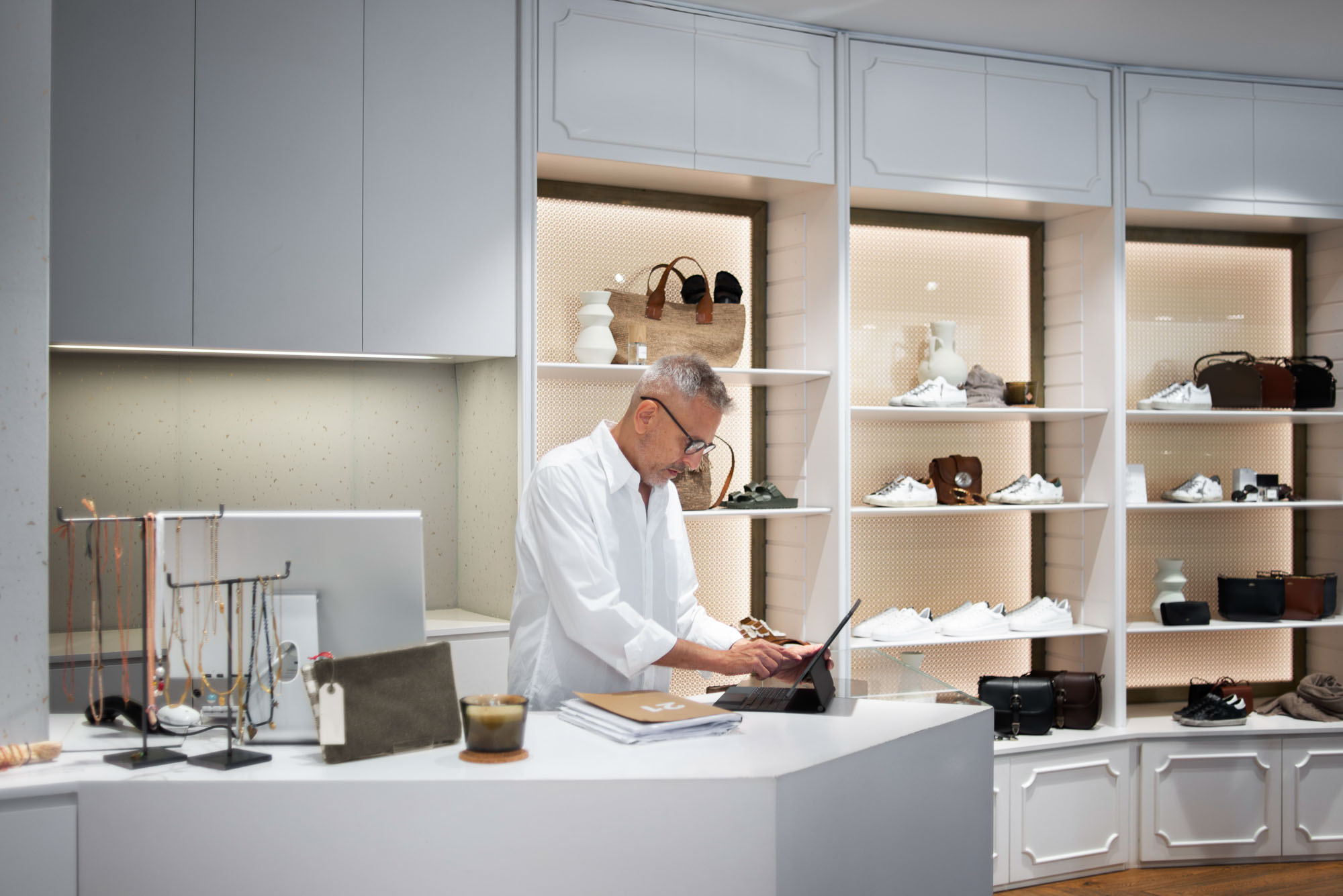 A man in a white shirt works on a tablet at a store's reception desk.